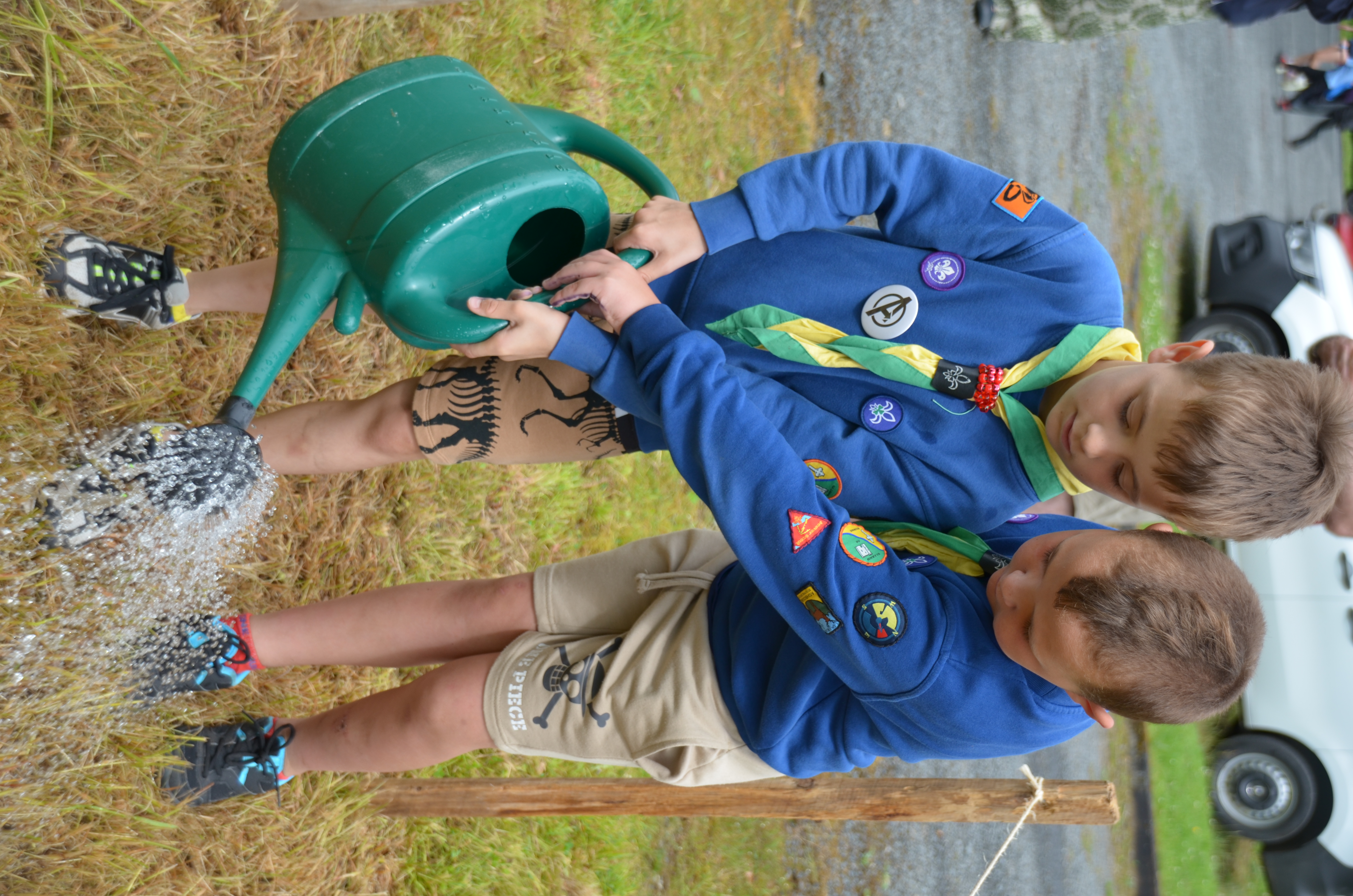 Two Cub Scouts hold a sprinkler while watering the soil.