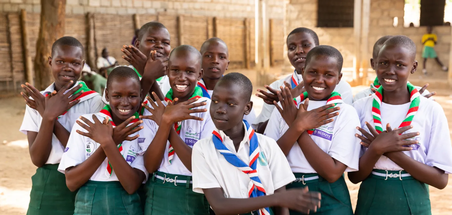 Scouts in a school in South Sudan in 2019 showing the Messengers of Peace hand sign