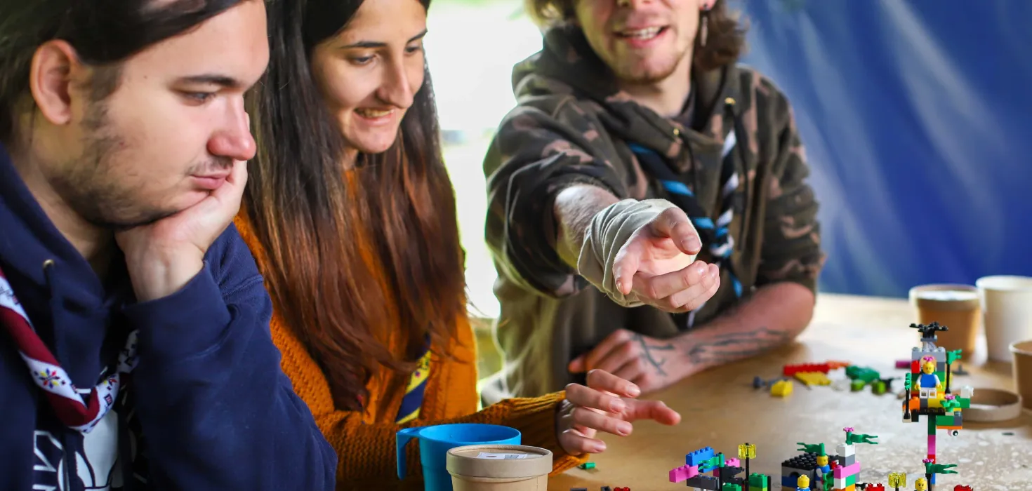 A Romanian Scout points at a lego structure while two other Scouts look at it.