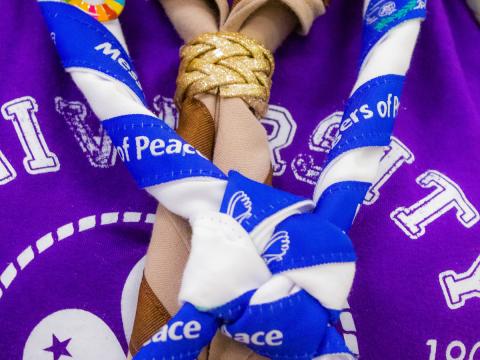 A closeup of a blue and white Messengers of Peace scout scarf worn by a scout girl