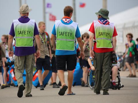 3 Scout Leaders walk away from the camera towards a group of Scouts, wearing Safety Vests