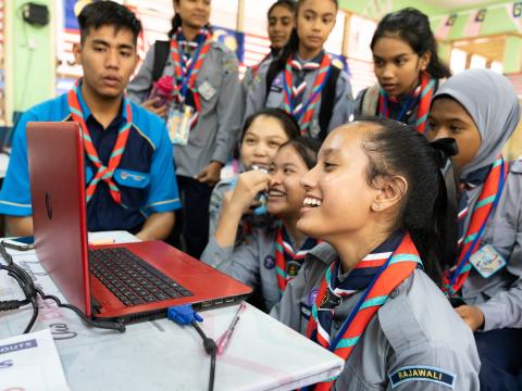 Un grupo de scouts malayos se ríe frente a un ordenador portátil mientras chatean por vídeo con scouts de otro país