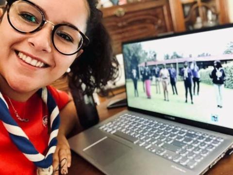 A Portuguese Scout wearing her scarf poses with a smile in font of her laptop while watching the JOTA-JOTI Live Show