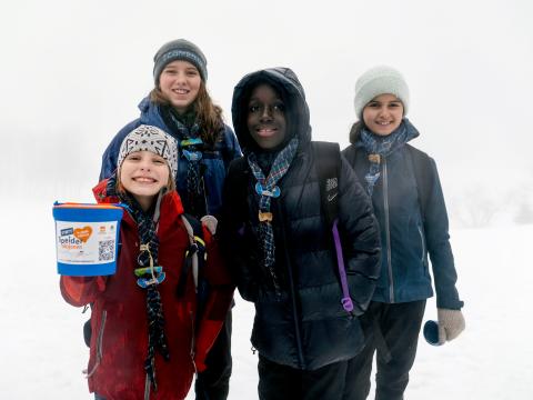 Quatre jeunes Scouts et Guides montrent une boîte utilisée pour récolter des fonds.