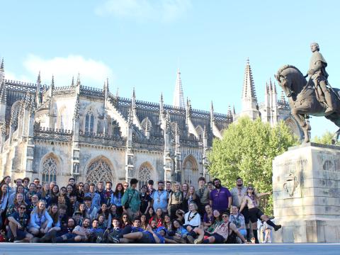 A group of young people wearing their Scout scarves stand in from of a church.