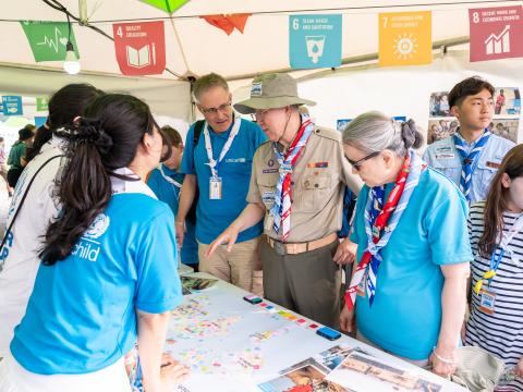 Scouts and UNICEF partners gather around a table in an SDG tent at the World Scout Jamboree while giving a tour to Mr. Ban Ki-moon