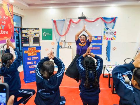Une séance de yoga en cours avec une consultante du Scoutisme Mondial à l'avant, et des étudiants qui suivent en levant les bras dans la pose de l'arbre. Ils participent à la partie mouvement du Défi de la santé mentale.