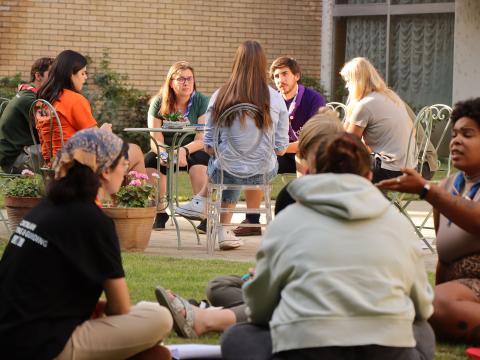 A group of people discuss while sitting on the grass.