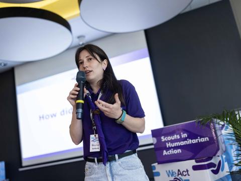 Raluca holds a microphone and presents during the WeAct Forum.