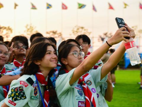 A group of Scouts at the 25th World Scout Jamboree pose in front of a phone to take a selfie at one of the celebrations. The Scouts are from the Singapore Scout Association