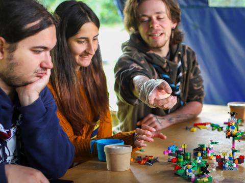 A Romanian Scout points at a lego structure while two other Scouts look at it.