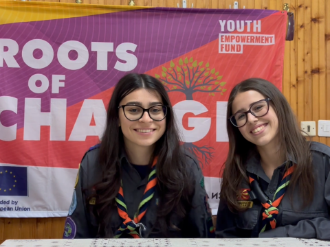 Two girls, wearing Scout scarves, smile at the camera.