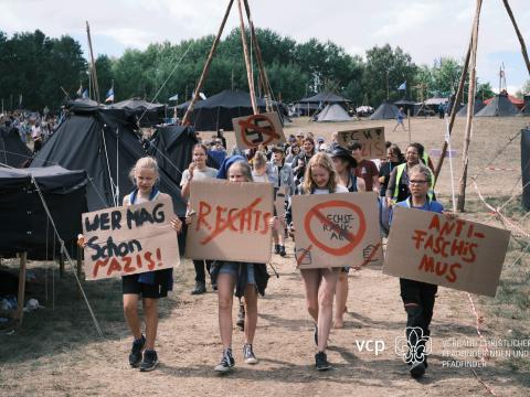 Scouts walk at a campsite holding banners.