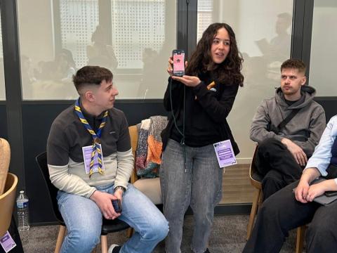 A young girl shows the screen of her phone while youth around her look at it.