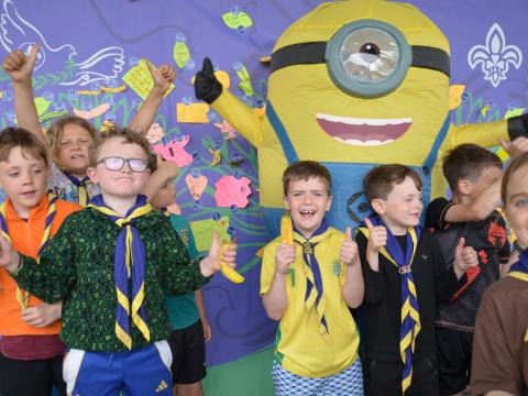 Children smile and hold bananas in front of a banner, together with someone in a minion costume.