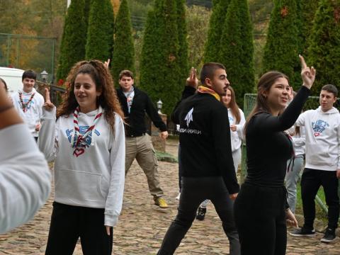 Young people wearing Scout scarves stand making two circles and gestures with their hands.