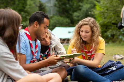 A small group of Scouts from different places sit on the grass together