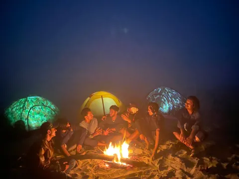 A group of boy Scouts in Bangladesh sit around the campfire at night next to their tents.