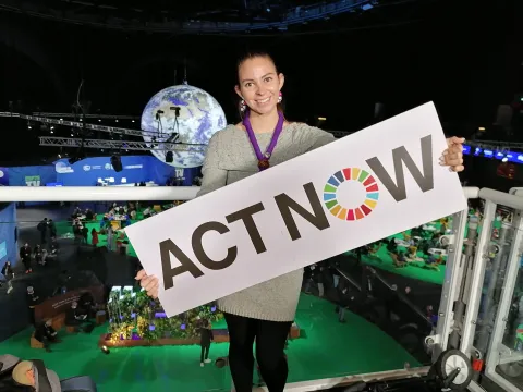 Grecia holds a sign reading "ACT NOW" with a giant planet structure behind her, during COP26