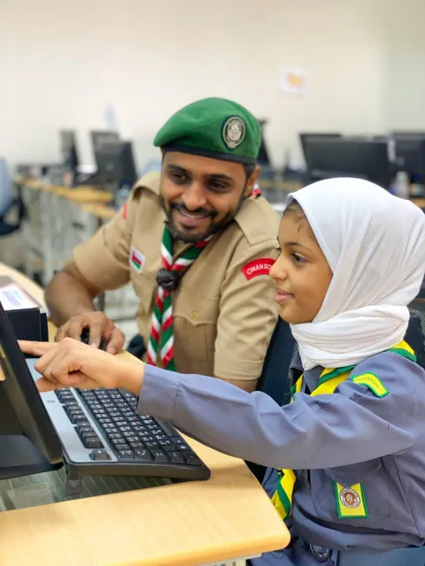 Un chef scout omanais assis devant un ordinateur avec une Scoute pendant le JOTA-JOTI 2021.
