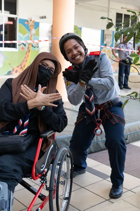 Two adult volunteers pose making a bird or dove shape with their hands, symbolising peace, during an annual JOTA-JOTI Scout event at a school in Kuala Lumpur, Malaysia