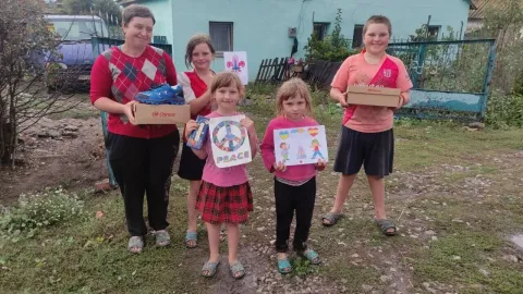 A Ukrainian family of four stand outside holding boxes of shoes they just received from Scouts in Spain