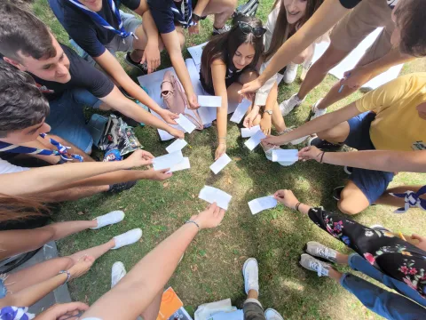A group of young Scouts make a circle and show small pieces of paper.