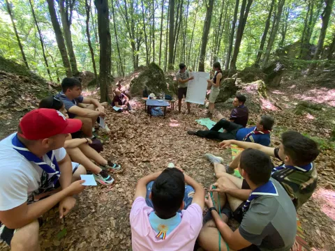 In the forest, young Scouts sit in a circle.