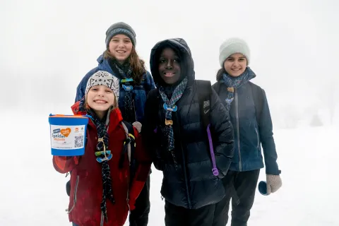 Four young Scouts and Guides stand showing a box used for raising funds.