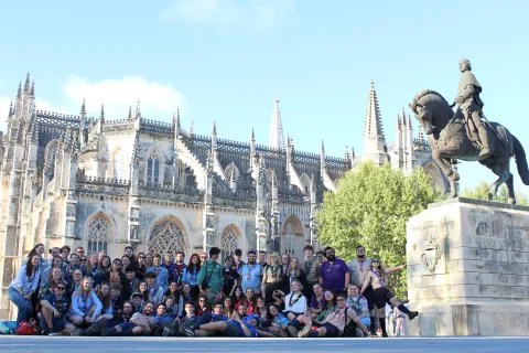 A group of young people wearing their Scout scarves stand in from of a church.