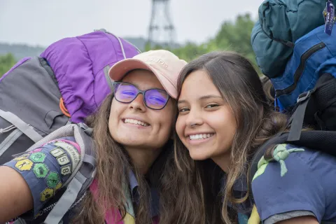 Two girl scouts have huge smiles as they arrive at the World Scout Jamboree and pose for a photo together with their huge backpacks on