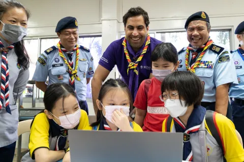 WOSM Secretary General Ahmad Alhendawi gathers around a computer with smiling Malaysian Scouts and Leaders during JOTA-JOTI, the largest annual digital Scouting event
