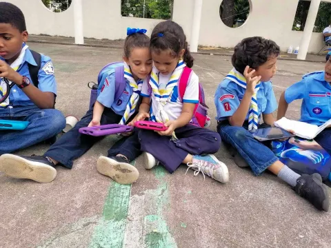 Young Scouts in the Dominican Republic sit on the ground while they check out JOTA-JOTI activities together on tablets