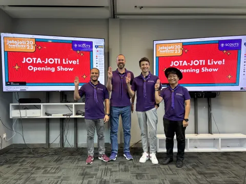 The WOSM World Events Team poses in front of two big television screens before the JOTA-JOTI Live opening show
