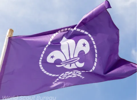 The purple WOSM flag flies with a blue sky in the background