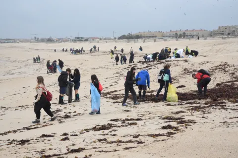 A beach with young people carrying plastic bags.