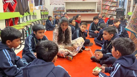 A circle of students seated on the floor, attentively engaged in a discussion with a teacher. The students look focused and involved in the mental health education of World Scouting’s pilot activities.