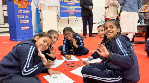 Des élèves en uniforme scolaire saluent la caméra alors qu'ils sont joyeusement occupés à colorier des mandalas sur le sol, dans le cadre de l'initiative « Santé et bien-être » des Scouts pour les ODD. Leurs expressions et leurs dessins colorés reflètent l'aspect créatif et thérapeutique de cette activité du Défi de la santé mentale.