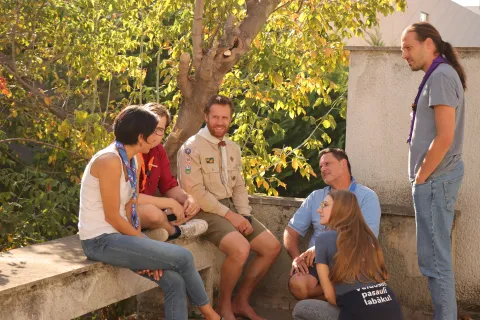 A group of people discuss under the shadow of a tree.