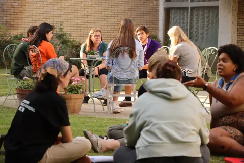 A group of people discuss while sitting on the grass.