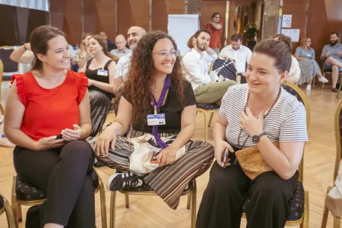 Inês sitting between two women, smiles.