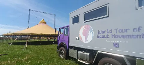 A purple truck with a custom sticker of a globe and the words 'World Tour of the Scout Movement' parked on a field.