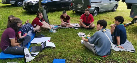 Young people and adults sit on the grass making a circle.