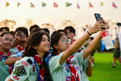 A group of Scouts at the 25th World Scout Jamboree pose in front of a phone to take a selfie at one of the celebrations. The Scouts are from the Singapore Scout Association