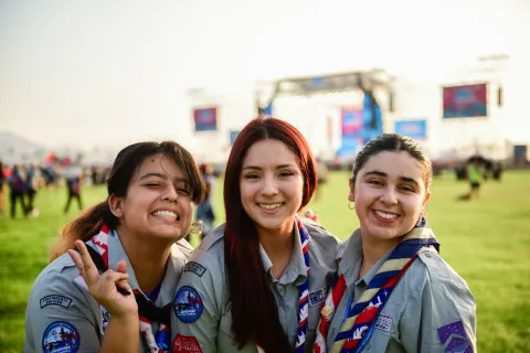 Tres niñas chilenas con su uniforme scout sonríen a la cámara.
