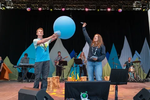 The presenters pop a blue balloon on stage.