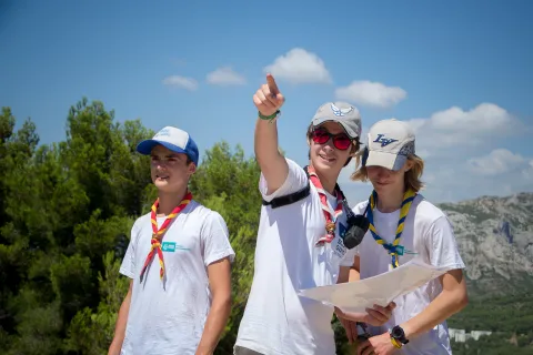 Three Scouts in nature. One of them holds a map and points out.
