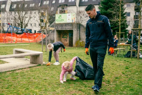 Children pick up trash from the floor under the supervision of an adult.