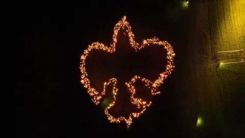 A fleur de lis made of candles, each of them held by a Scout.