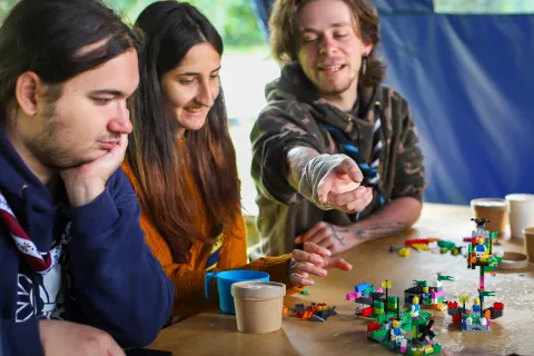 A Romanian Scout points at a lego structure while two other Scouts look at it.